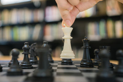 Cropped hand of woman playing chess on table in library