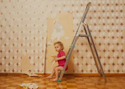 Child tear off the wallpaper from the wall in the room, little mother's helper