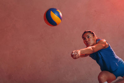 Young woman playing volleyball against wall