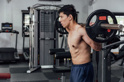 Shirtless man lifting dumbbell in gym