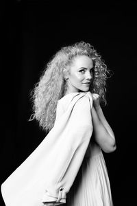 Portrait of woman with curly hair standing against black background