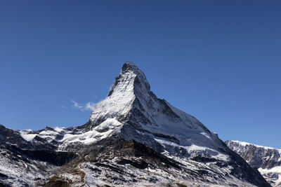 Low angle view of snowcapped mountains against clear blue sky