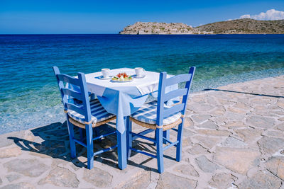 Chairs on table by sea against blue sky