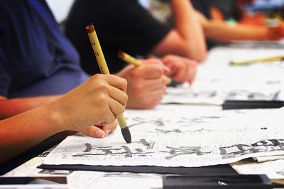 Midsection of children writing on books in classroom