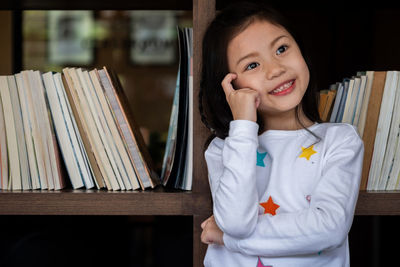 Thoughtful smiling girl standing against bookshelf