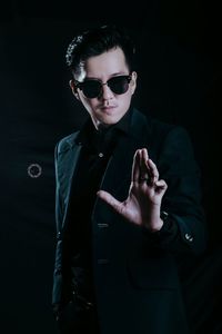 Portrait of young man wearing sunglasses standing against black background
