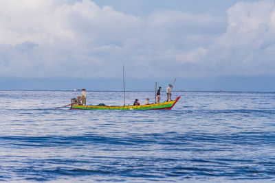 People on boat sailing in sea against cloudy sky
