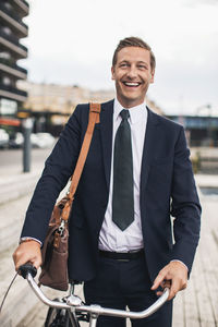 Smiling businessman standing with bicycle in city