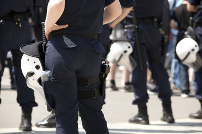 Rear view midsection of female police officer standing with hand on hip