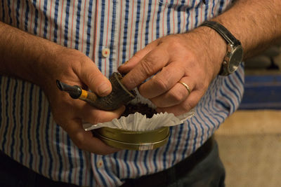 Midsection of man filling tobacco in smoking pipe