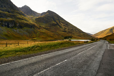 Road leading towards mountains against sky in scotland