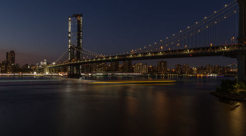 Illuminated bridge over river in city at night