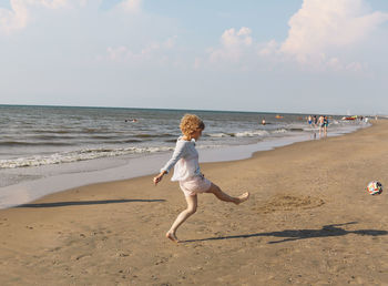 Side view of woman playing at beach against sky