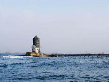 Lighthouse by sea against clear sky