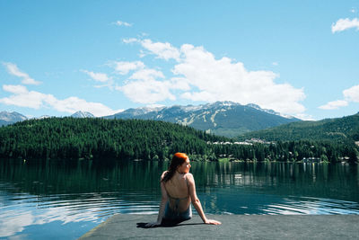 Rear view of woman sitting against calm lake