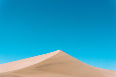 Low angle view of sand dunes against clear blue sky