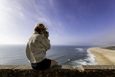 Woman sitting on shore at beach against sky