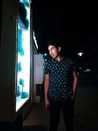 Portrait of young woman standing against illuminated wall