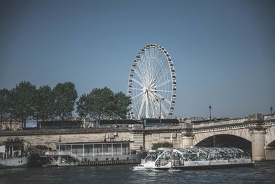 Ferris wheel by river against clear sky