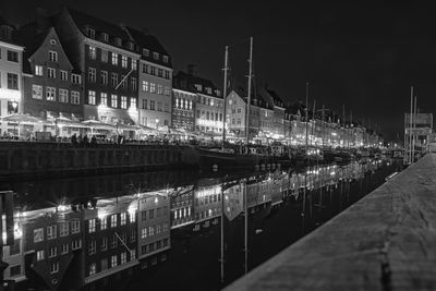 Illuminated buildings by river against sky in city at night