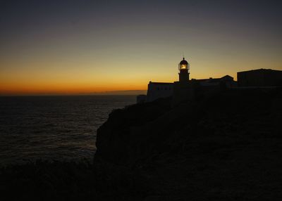 Silhouette buildings by sea against sky during sunset