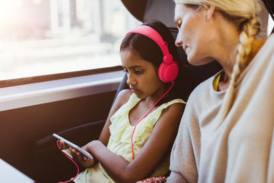 Mother looking at daughter watching movie on smart phone while traveling in train