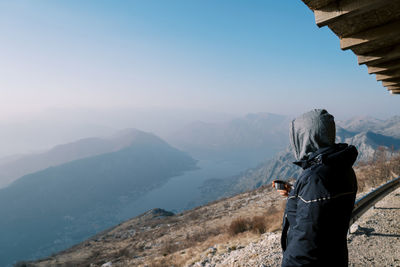 Rear view of man standing on mountain against clear sky