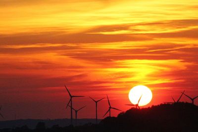 Silhouette of wind turbines on landscape against sunset sky