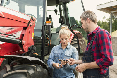 Man and woman holding equipment while standing by tractor at farm