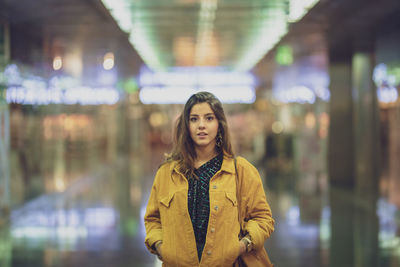 Portrait of young woman standing in corridor of illuminated mall