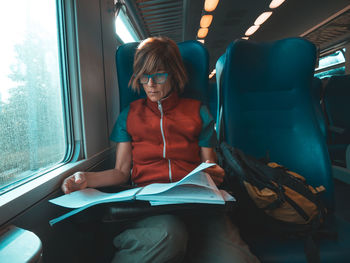 Mature woman reading book while traveling in train