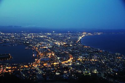 Aerial view of illuminated cityscape by sea against sky at night