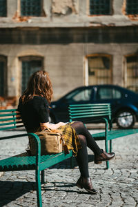 Young european woman in yellow chequered skirt sitting on a green metal bench while social distancin