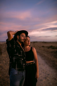 Young couple standing on land against sky during sunset