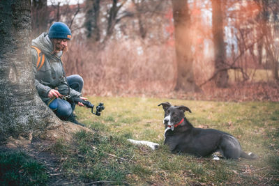 Young woman photographing dog sitting on grassy field in forest