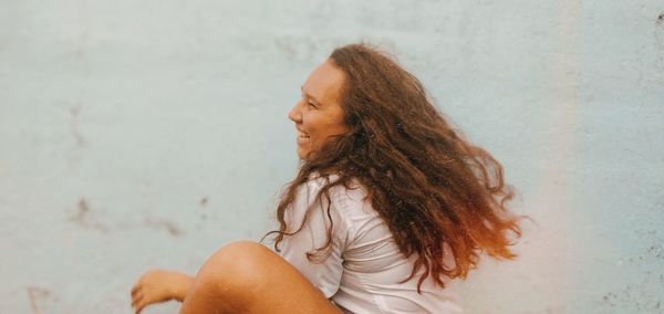 Side view of happy woman sitting against wall