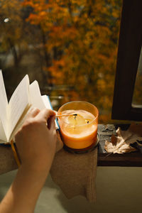 Hand with burning match lighting a candle on the windowsill with autumn decor