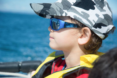 Close-up of boy wearing sunglasses and cap in boat on sea