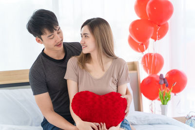 Couple holding red heart shaped balloons