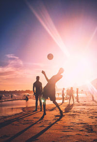 People playing with ball on beach during sunset