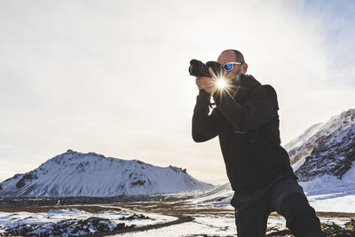 Man photographing on snowcapped mountain against sky