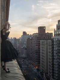 Woman standing by buildings in city against sky during sunset