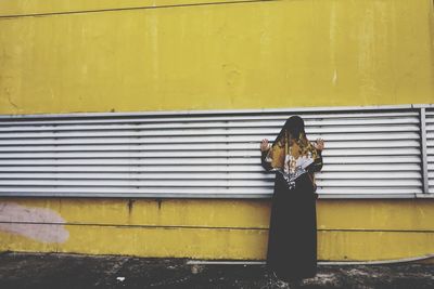 Rear view of woman standing on yellow wall