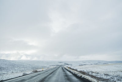 Road amidst snow covered field against sky during winter