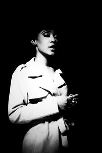 Young woman smoking cigarette against black background