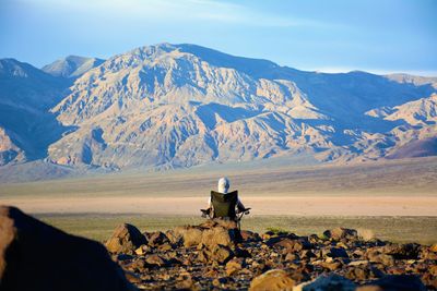 Rear view of man sitting on mountain against sky