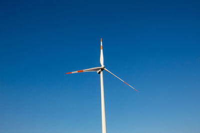 Low angle view of wind turbine against clear blue sky