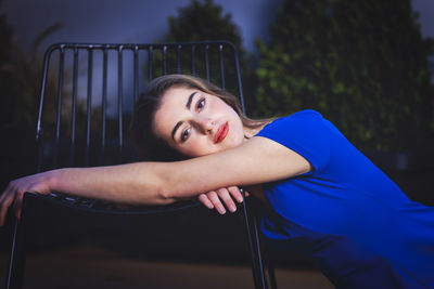 Portrait of young woman sitting by chair outdoors