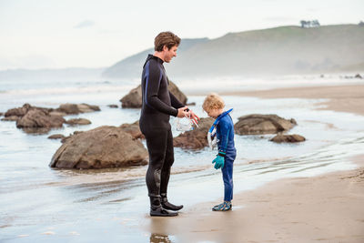 Father and son in wetsuits on beach in new zealand