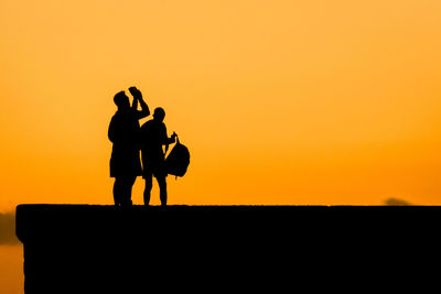 Silhouette man photographing on orange sky